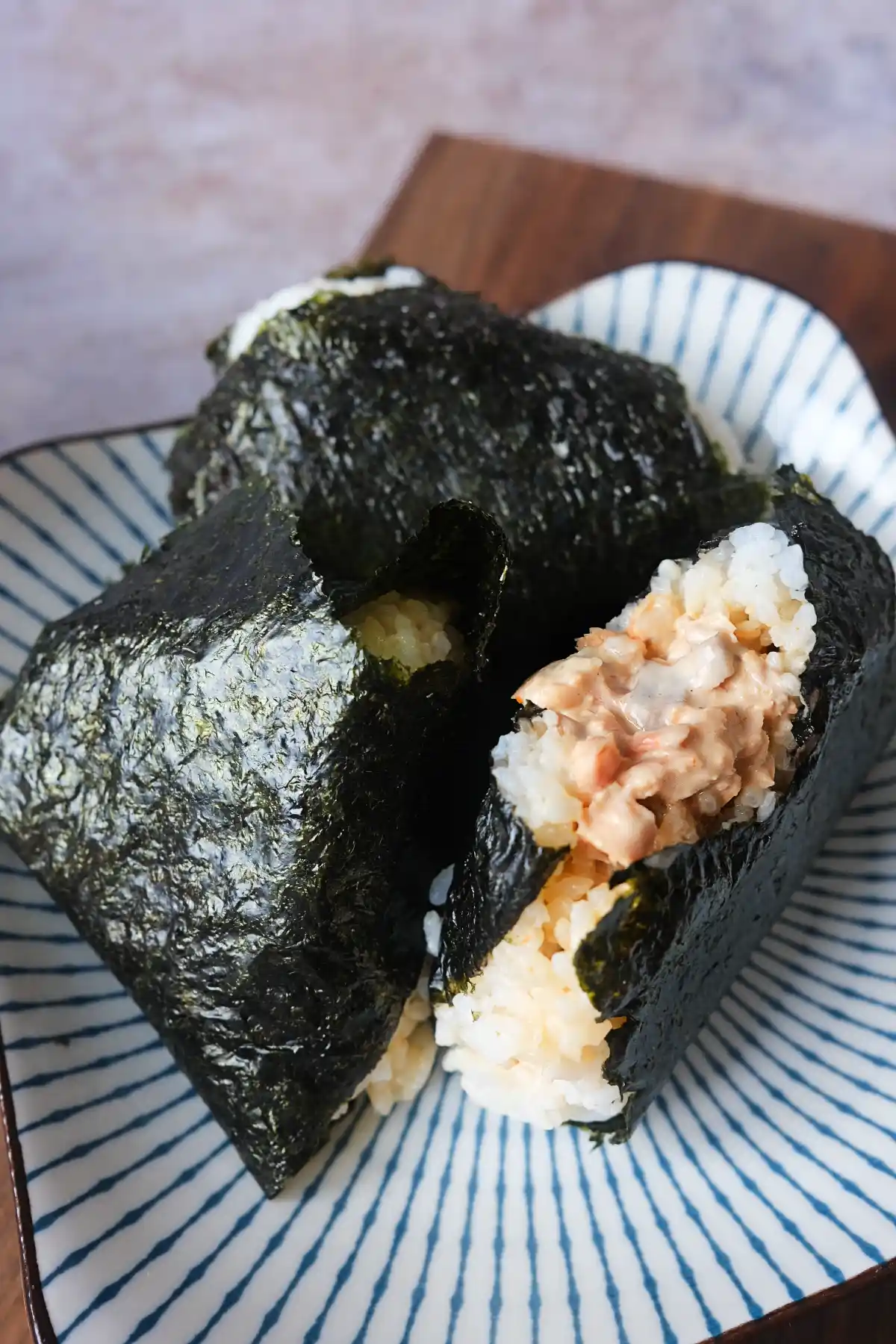 Salmon onigiri wrapped in nori on a plate with one rice ball opened to reveal a creamy salmon filling