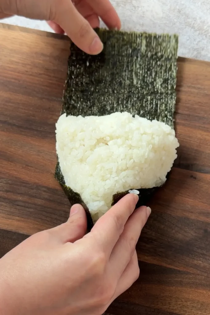Folding nori around a salmon onigiri to secure the rice ball and filling