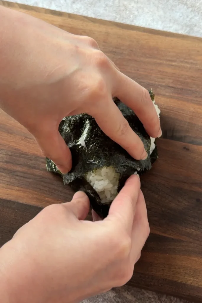 Hands pressing nori around a homemade salmon onigiri to secure the seaweed wrapper
