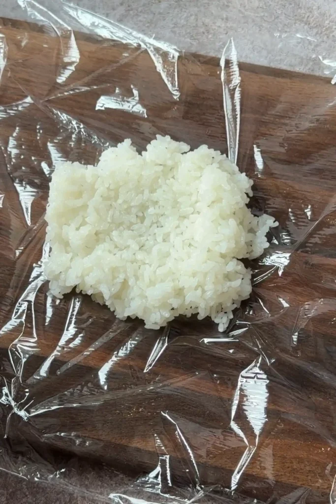 Warm Japanese short-grain rice spread on plastic wrap for shaping salmon onigiri