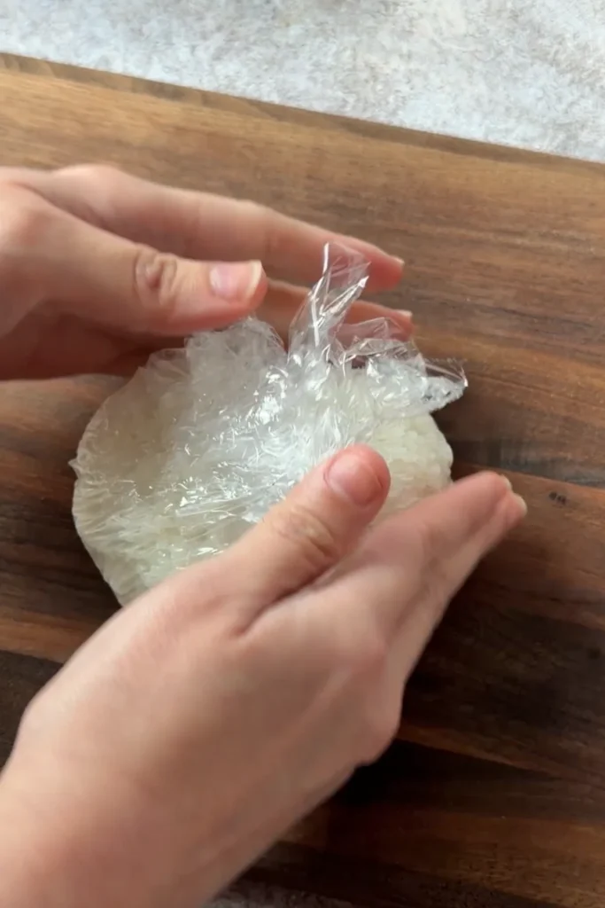 Shaping salmon onigiri with plastic wrap into a traditional triangle rice ball