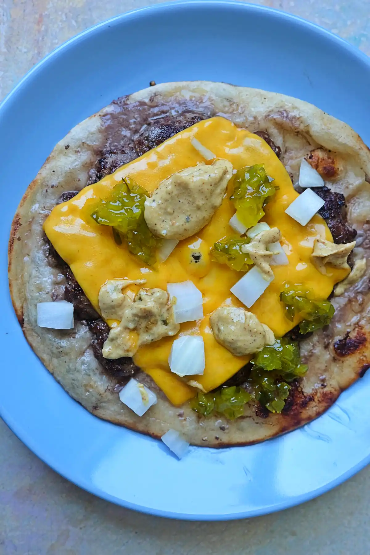Smash burger taco topped with melted American cheese, onions, pickles, and burger sauce