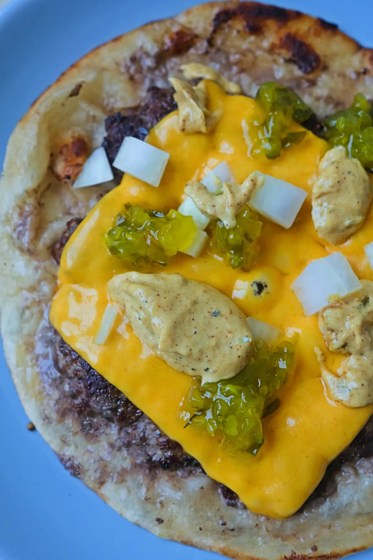 Close-up of smash burger taco with melted cheese, diced onions, and pickle relish
