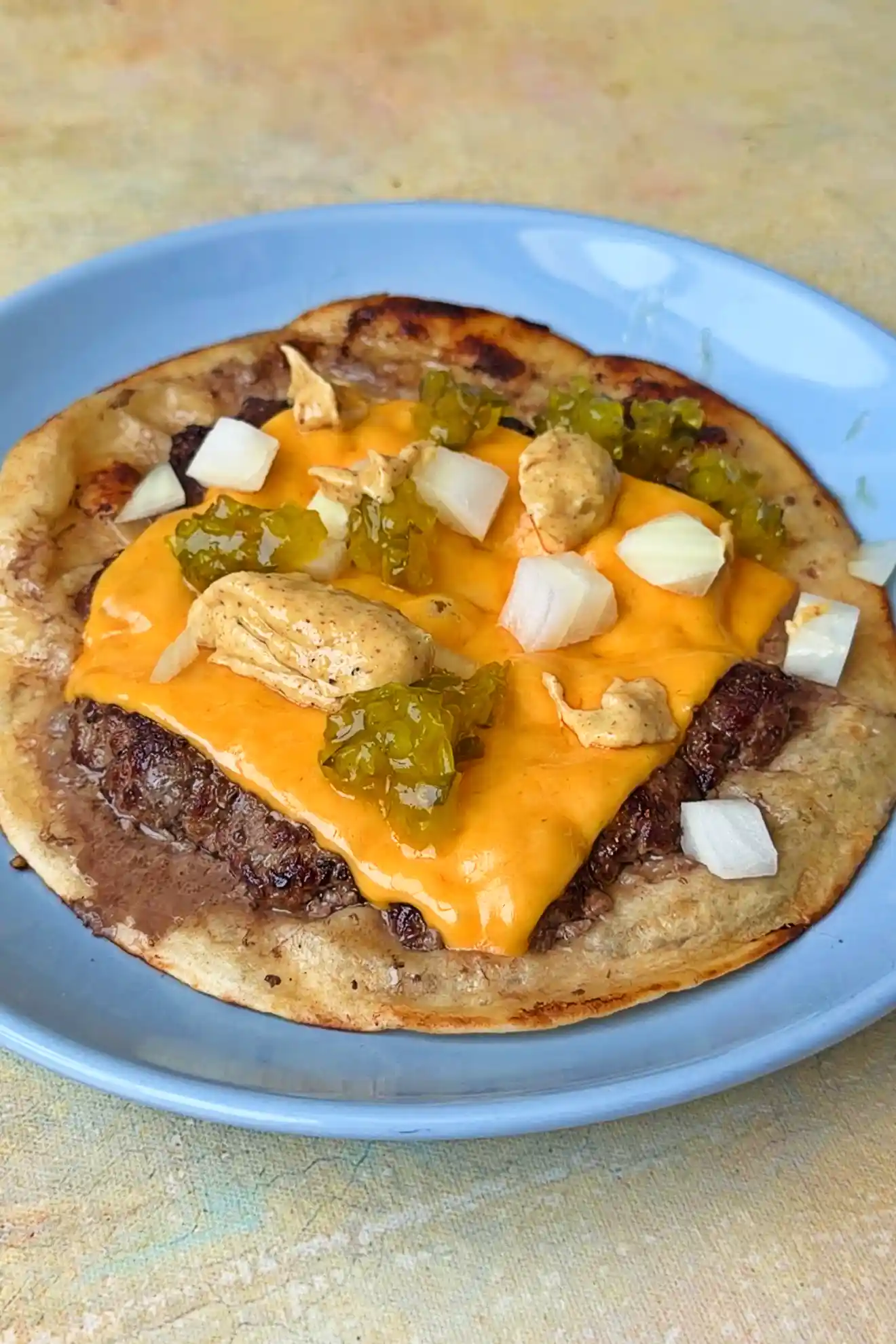 Finished smash burger taco with melted cheese, burger sauce, onions, and pickles ready to serve