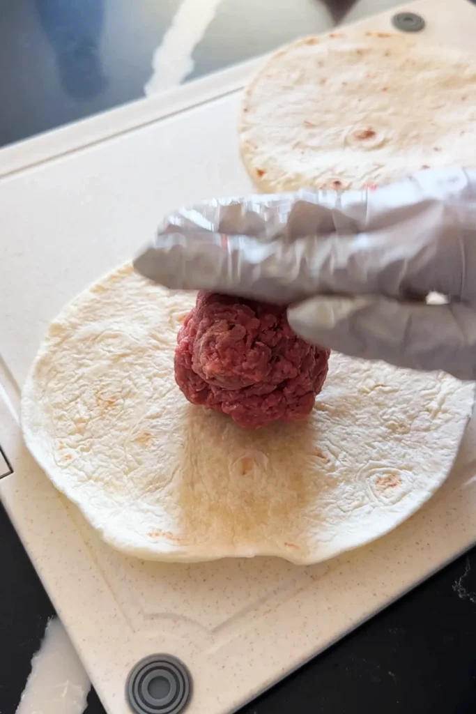 Pressing ground beef onto a flour tortilla for smash burger tacos