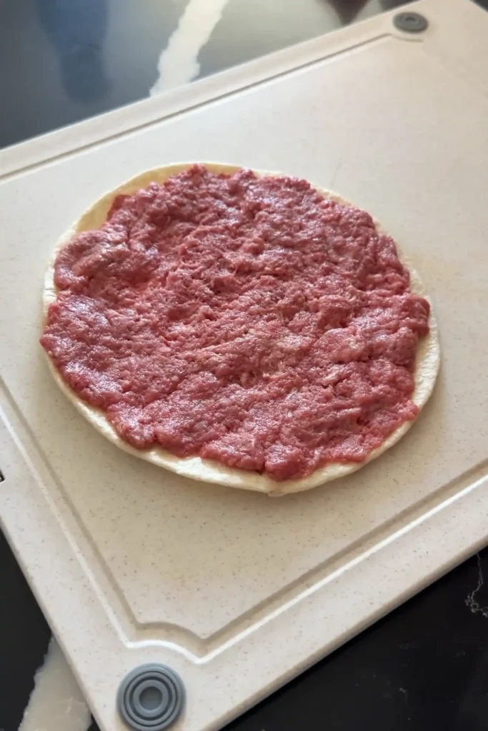 Ground beef spread evenly across a flour tortilla for smash burger tacos