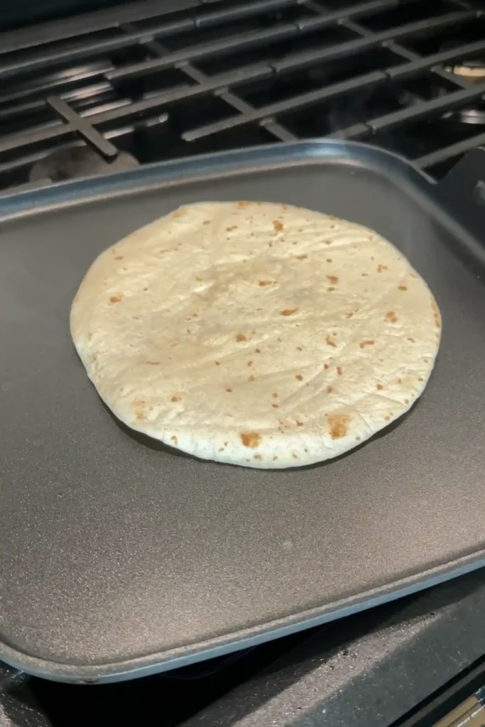 Flour tortilla cooking on a hot griddle for smash burger tacos