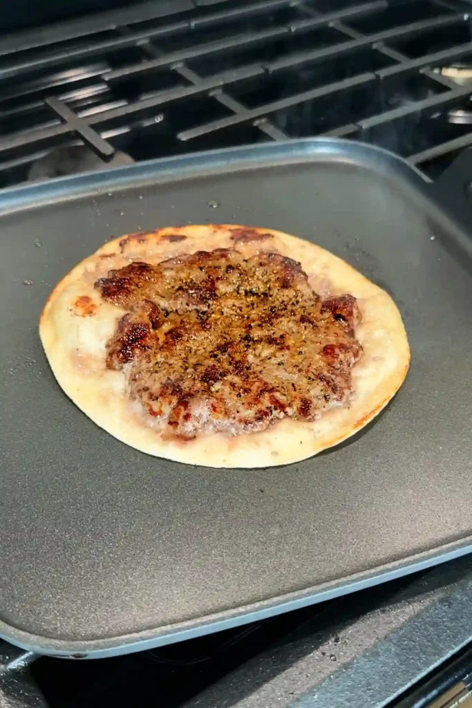 Crispy smash burger taco cooking on a griddle after flipping