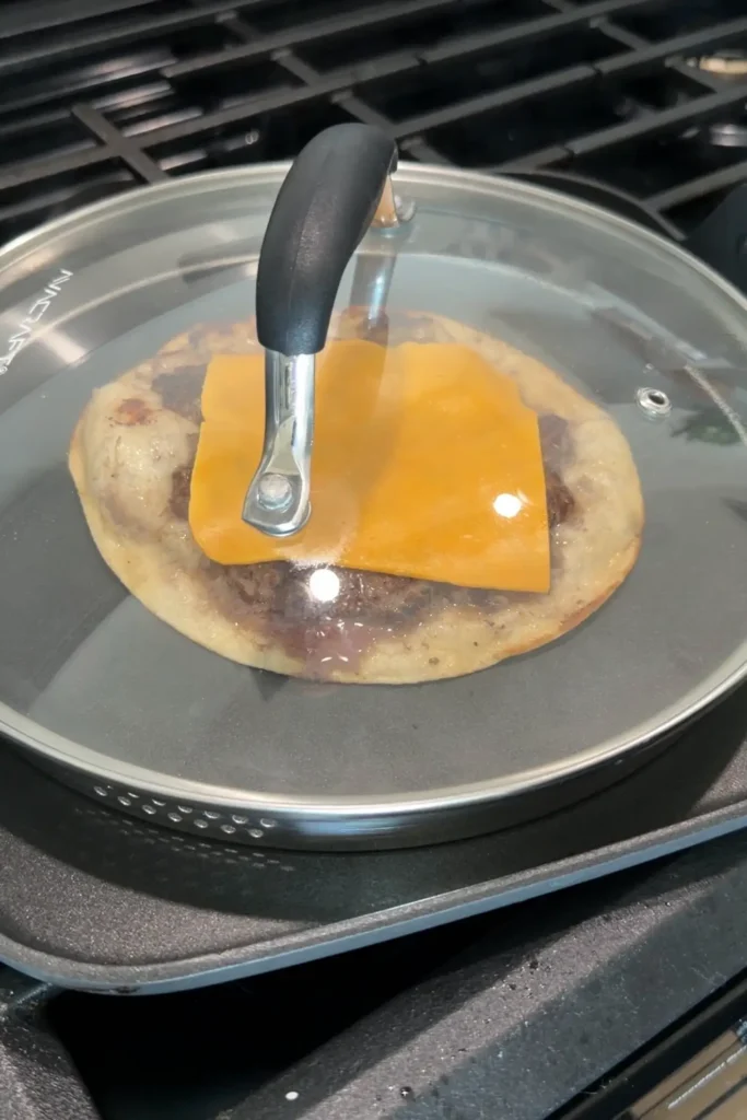 Melting American cheese on a smash burger taco under a lid