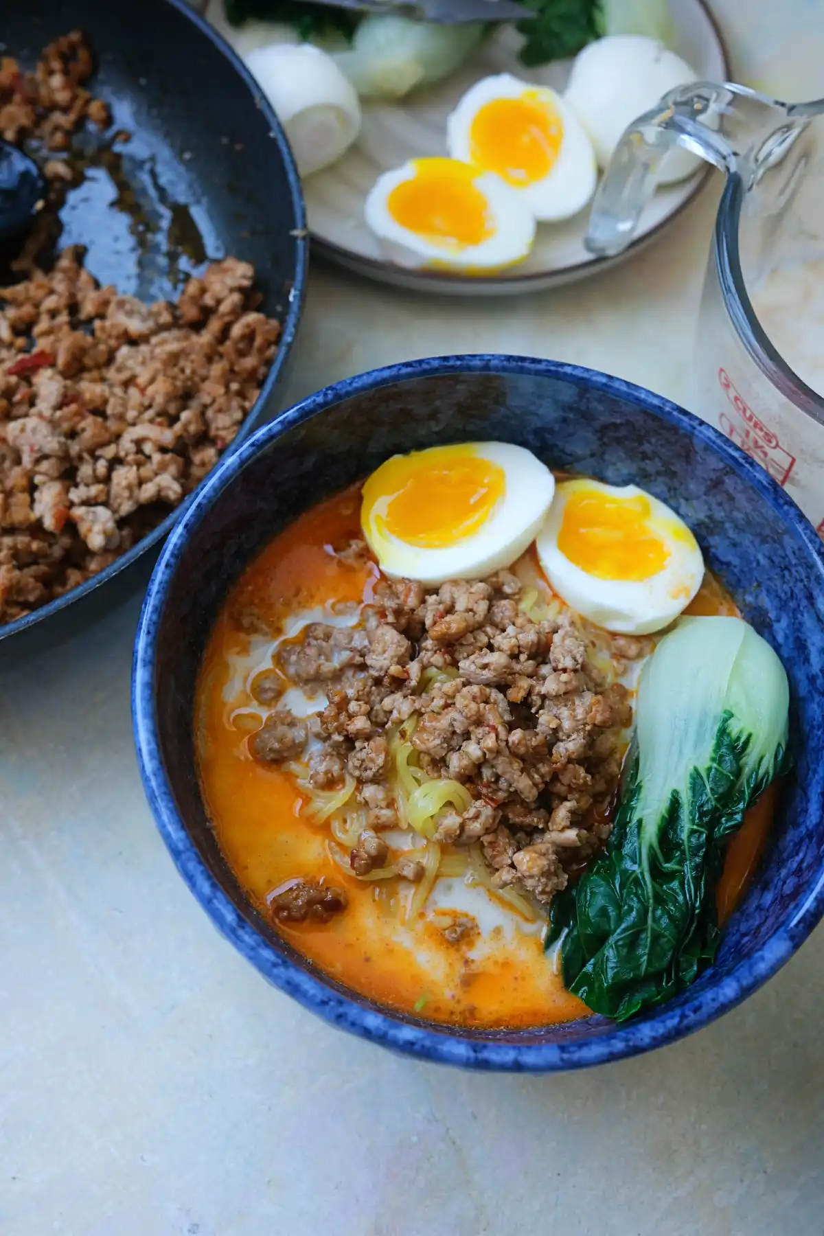 Japanese tantanmen ramen served in a blue bowl with sesame broth, pork topping, bok choy, and jammy eggs