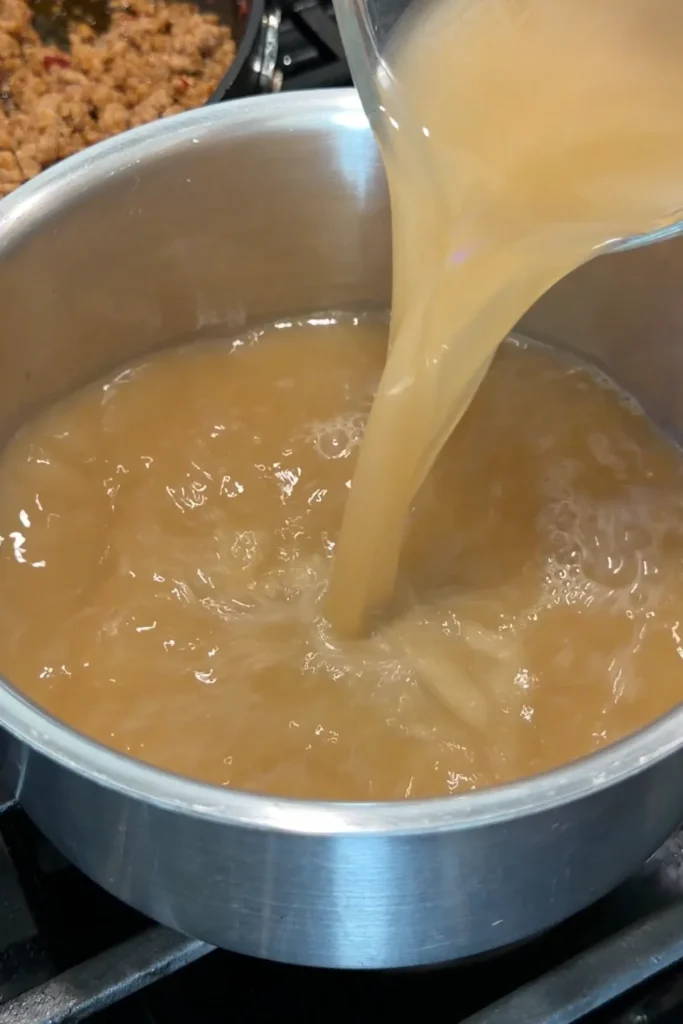 Dashi broth being poured into a saucepan for creamy tantanmen ramen