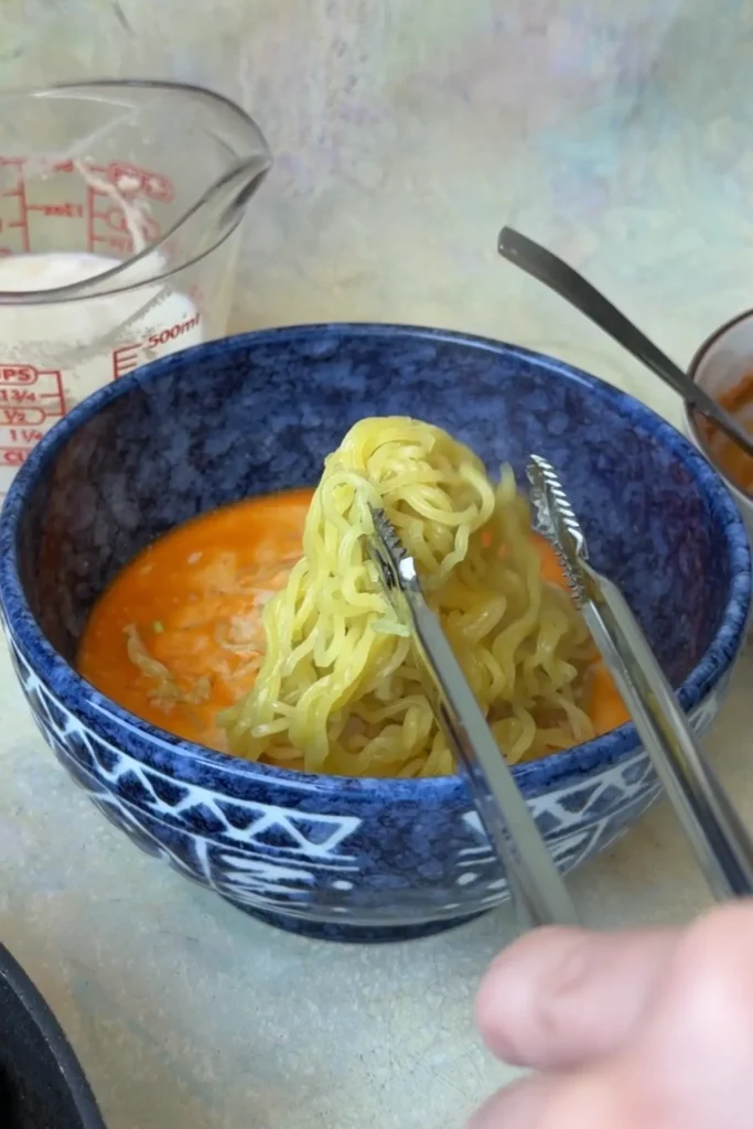 Cooked ramen noodles being added to creamy sesame broth for homemade tantanmen