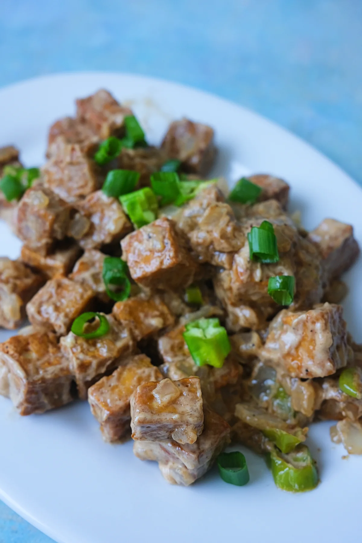Tofu sisig served on a white plate, topped with green onions and chopped chiles.