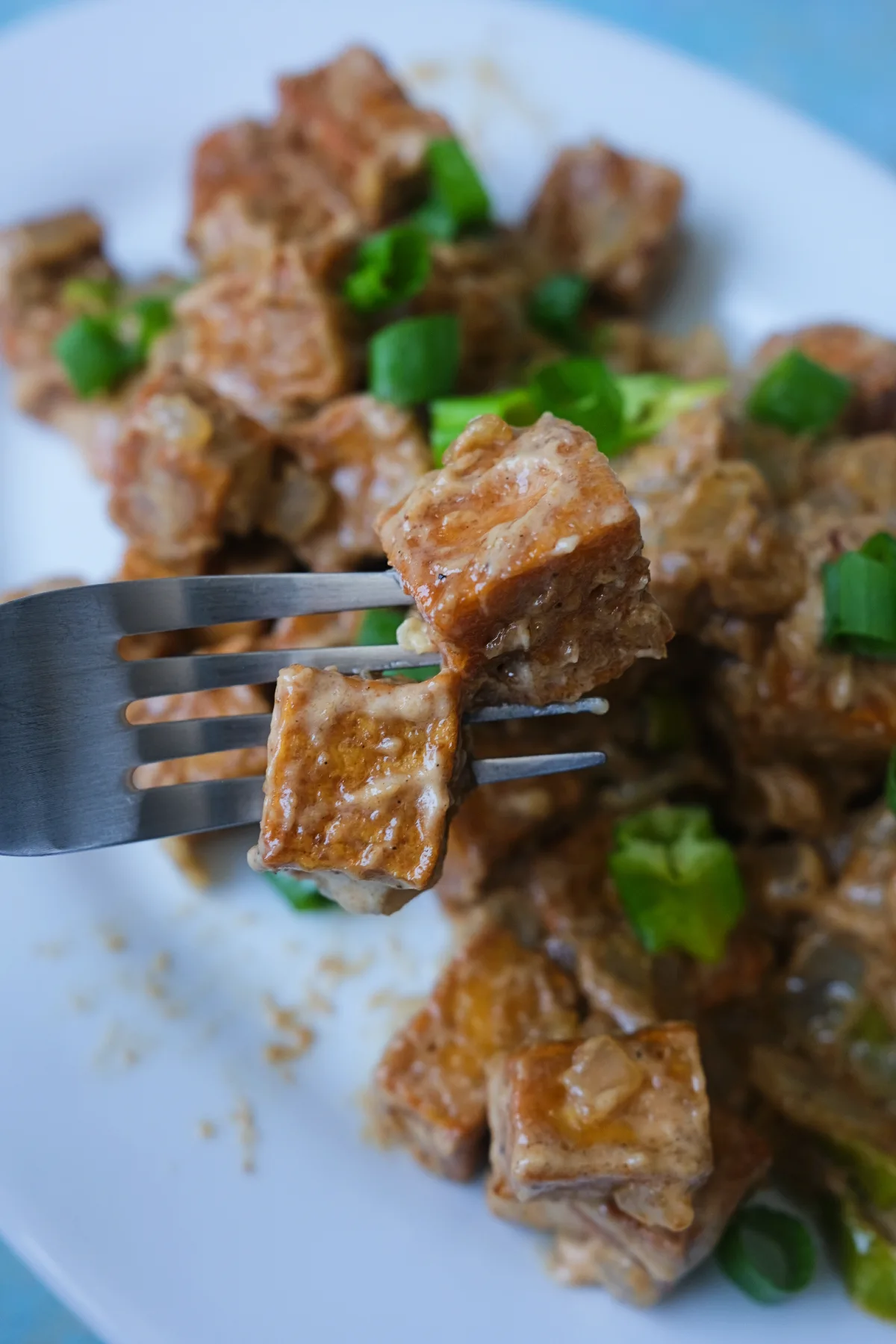 Fork holding a bite of crispy tofu sisig coated in creamy sisig sauce with onions and chiles.
