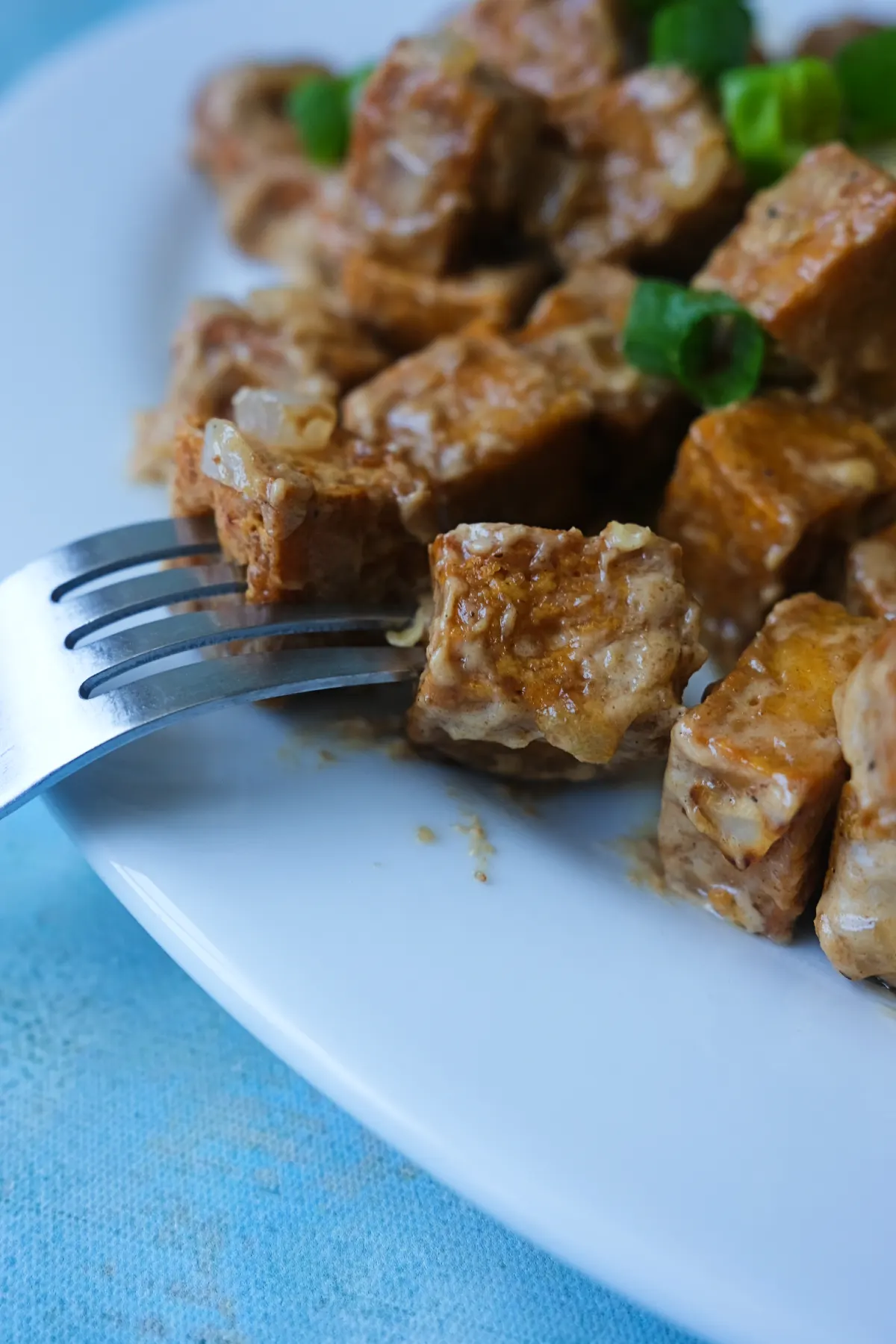 Close-up of tofu sisig garnished with green onions and sliced green chiles.
