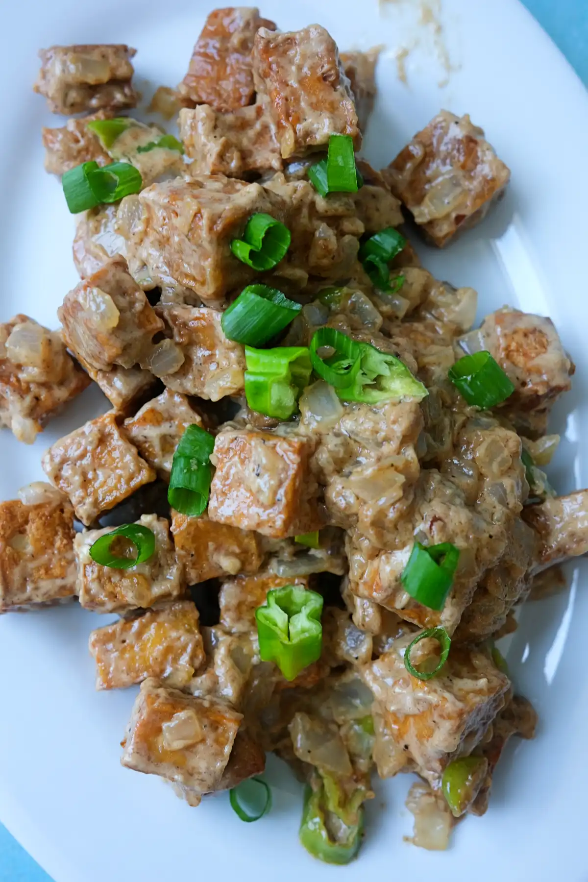 Overhead view of tofu sisig with crispy tofu cubes, creamy sauce, onions, and chiles.