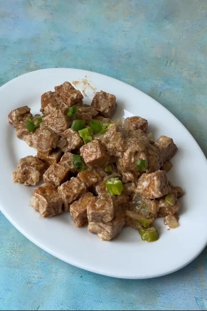 Homemade tofu sisig plated and garnished with green onions and chiles.