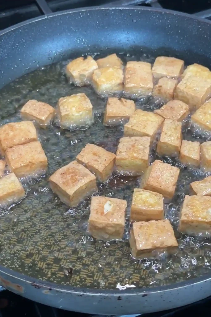 Golden brown tofu cubes frying in oil until crispy.