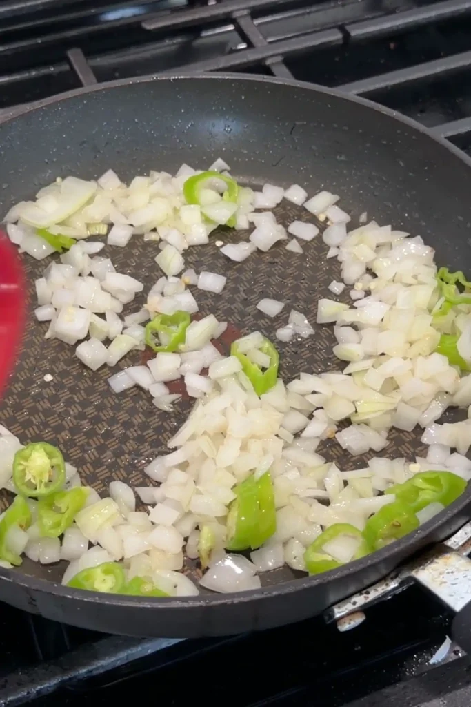Diced onions and sliced green chiles sautéing in a skillet.