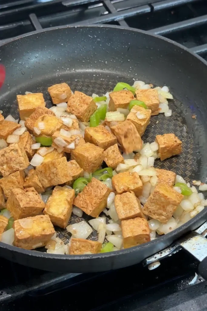 Crispy fried tofu added to sautéed onions and chiles in a skillet.