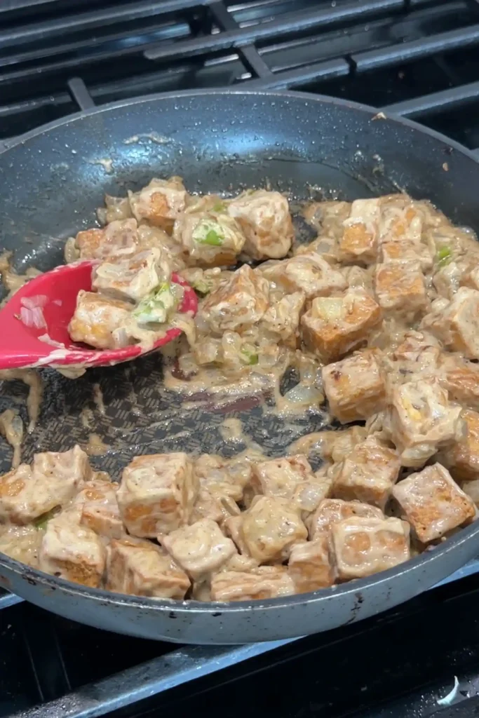 ofu sisig tossed in creamy sauce with onions and chiles in a skillet.