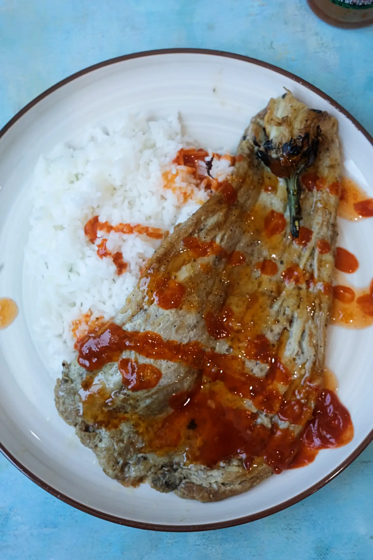 Close-up of tortang talong topped with sweet banana ketchup beside white rice.
