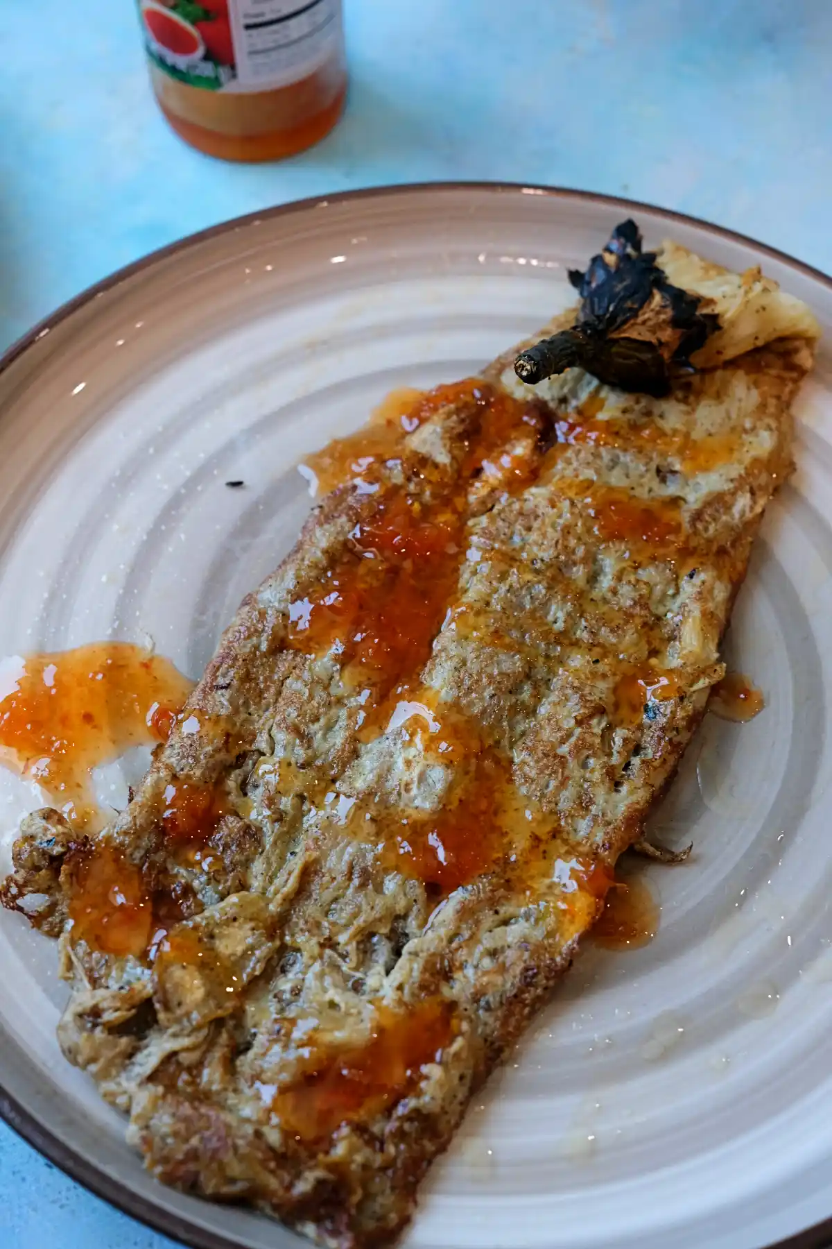 Crispy golden tortang talong drizzled with banana ketchup on a serving plate.