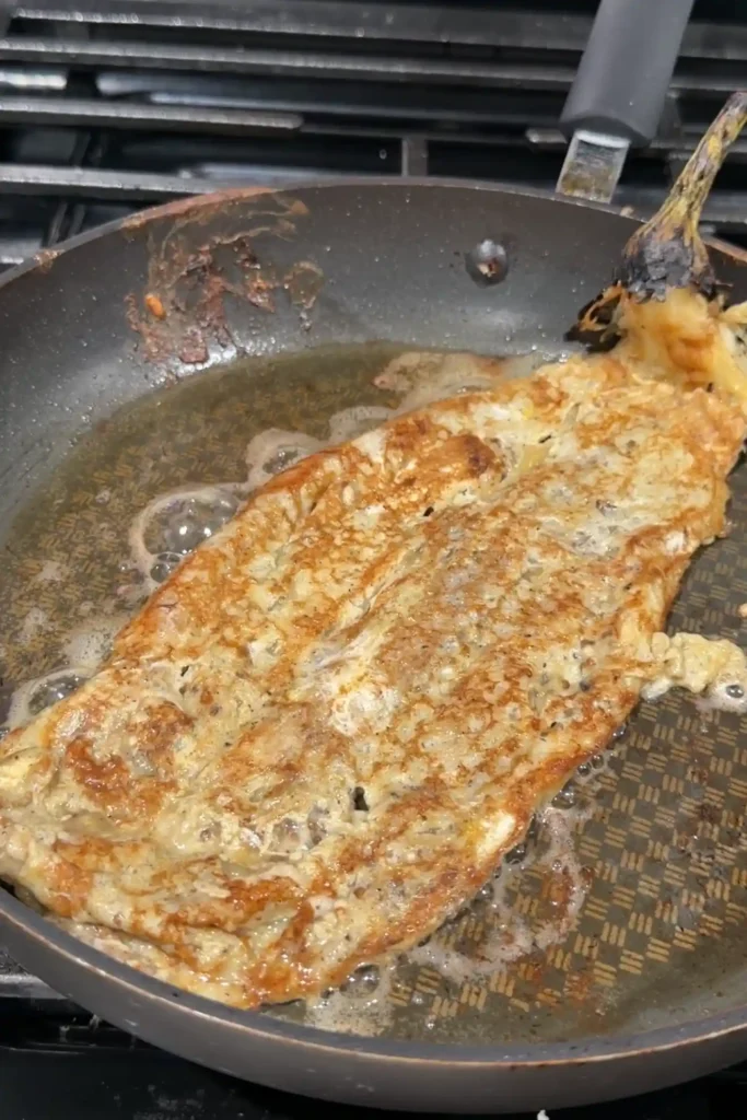 Tortang talong frying in oil until golden brown and crisp around the edges.