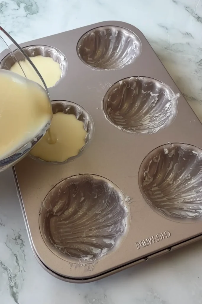Butter tteok batter being poured into the cavities of a buttered madeleine pan.