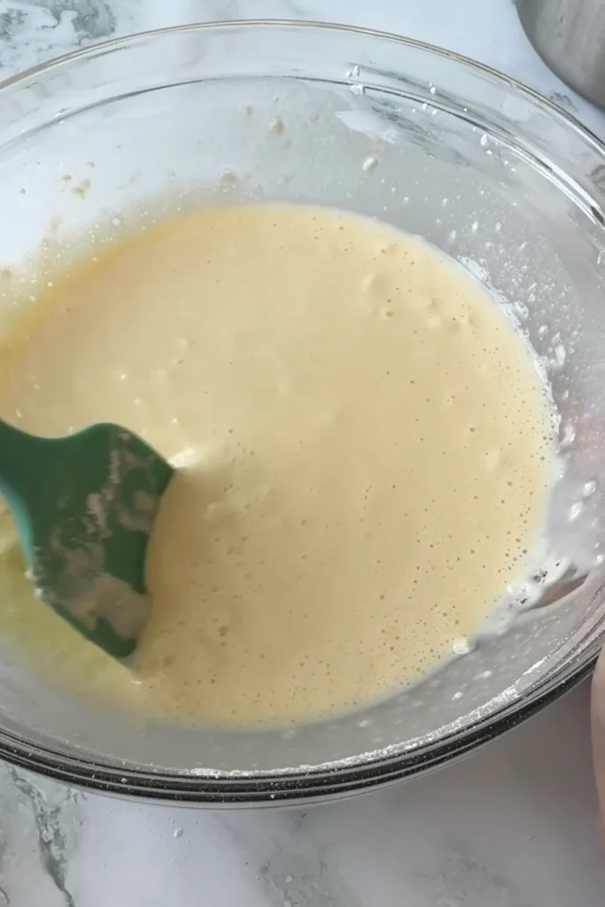 Smooth butter tteok batter in a glass mixing bowl after mixing.