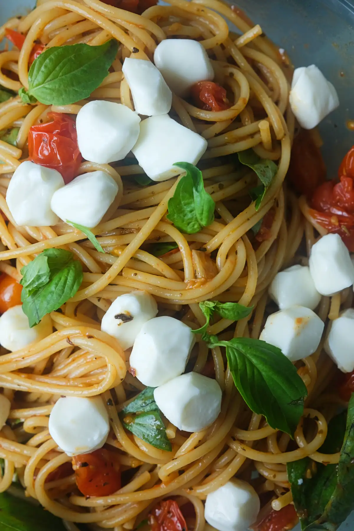 Spaghetti tossed with blistered cherry tomatoes, fresh basil leaves, and mozzarella pearls in a large serving bowl.