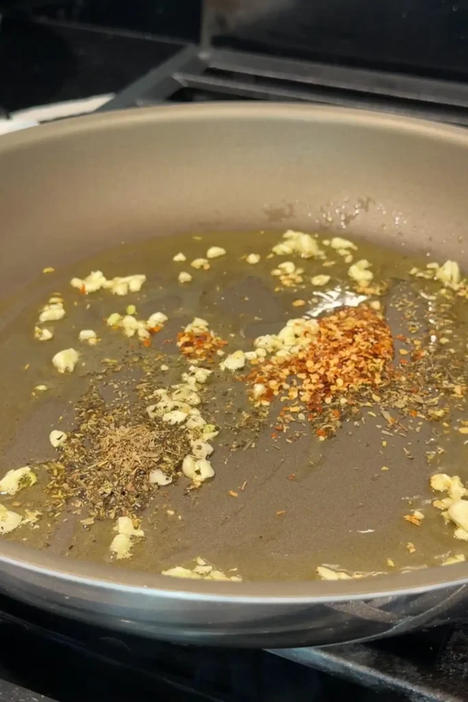 Olive oil, minced garlic, Italian seasoning, crushed red pepper flakes, and black pepper cooking in a skillet.