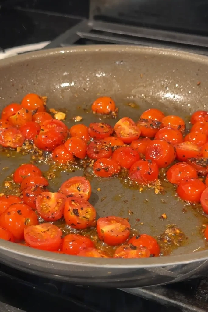 Cherry tomatoes cooking until softened and beginning to blister in the skillet.