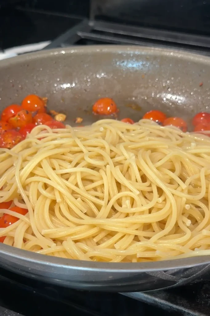Cooked spaghetti added to the skillet with the blistered cherry tomatoes.