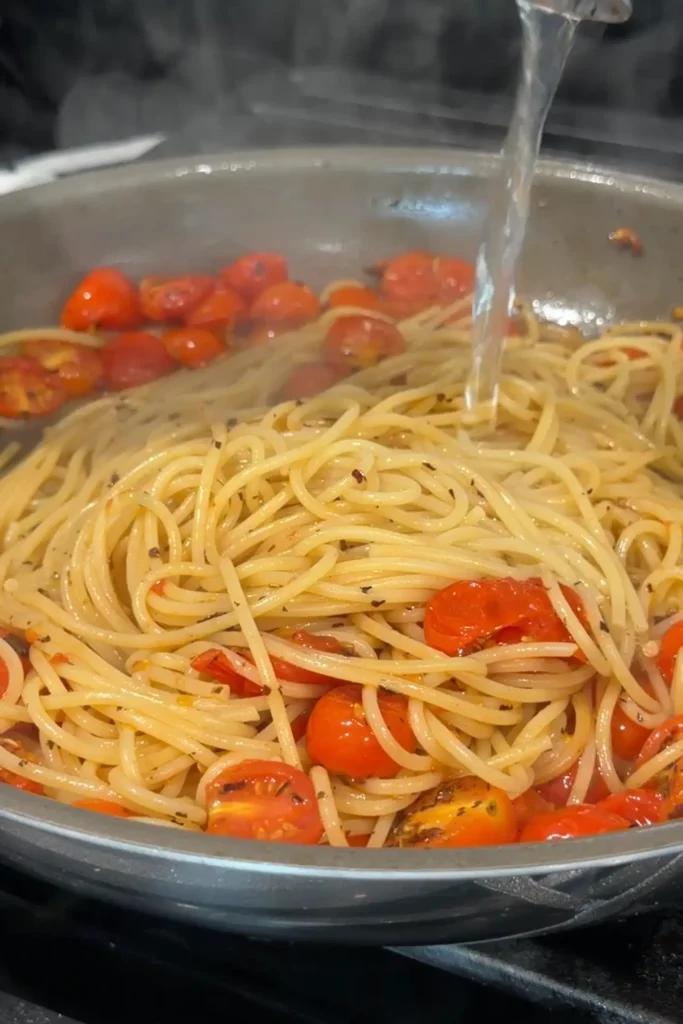 Reserved pasta water being poured into the skillet with the spaghetti and tomatoes.