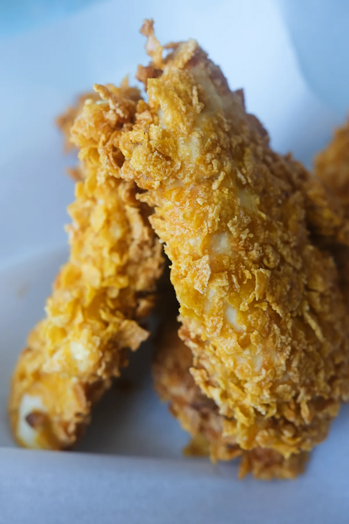 Cornflake chicken tenders arranged in a paper-lined dish with a golden, crispy cornflake coating.