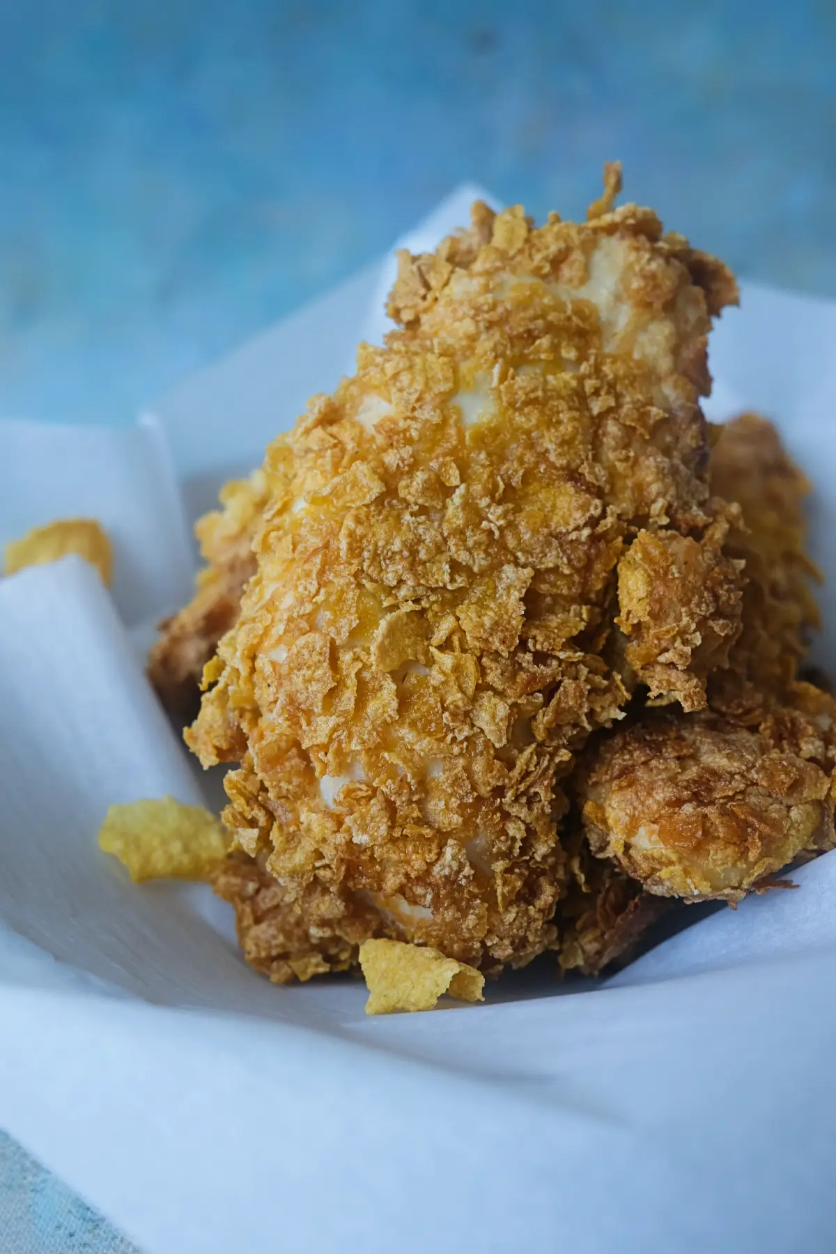 Crispy cornflake chicken tenders served in a paper-lined dish with loose cornflake crumbs.