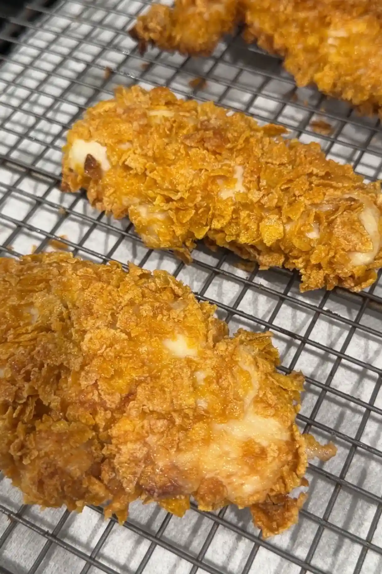Fried cornflake chicken tenders resting on a wire rack after cooking.