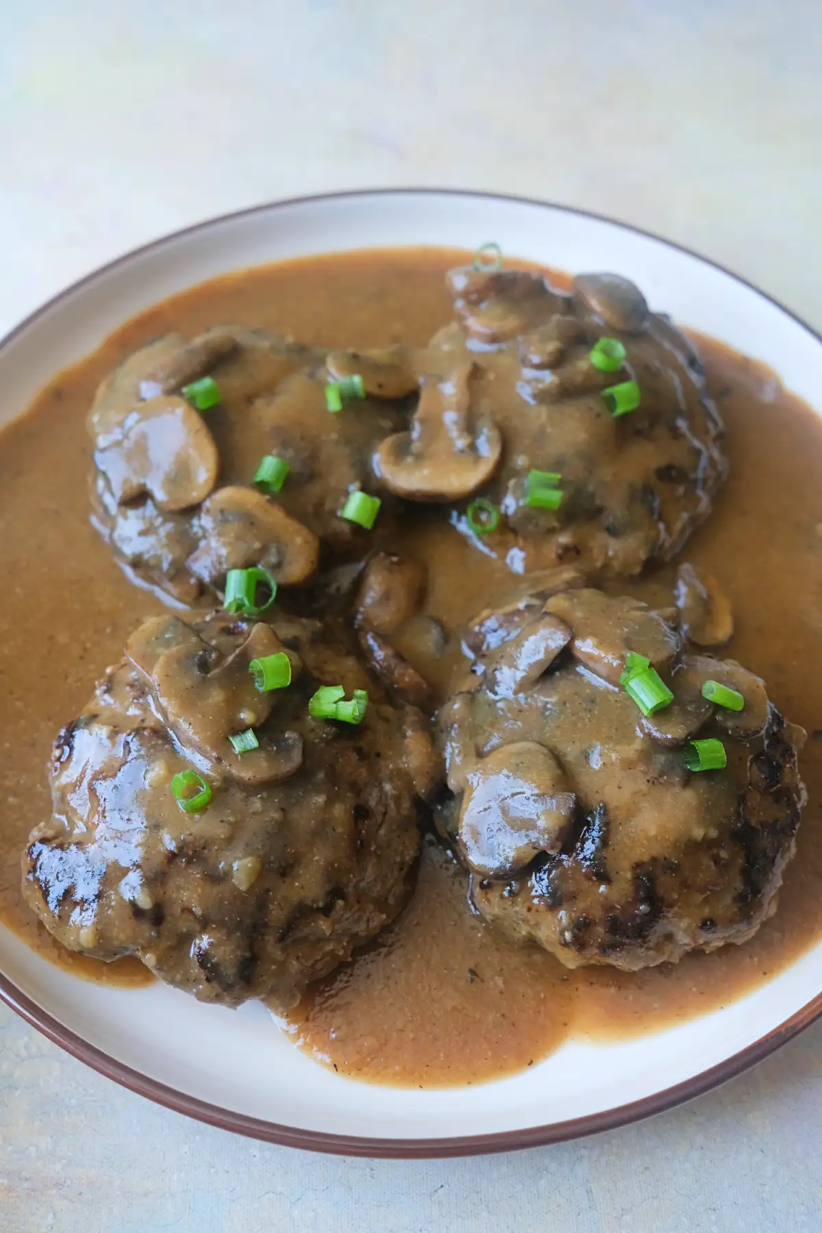 Homemade hamburger steak with mushroom gravy topped with fresh green onions and served on a plate.
