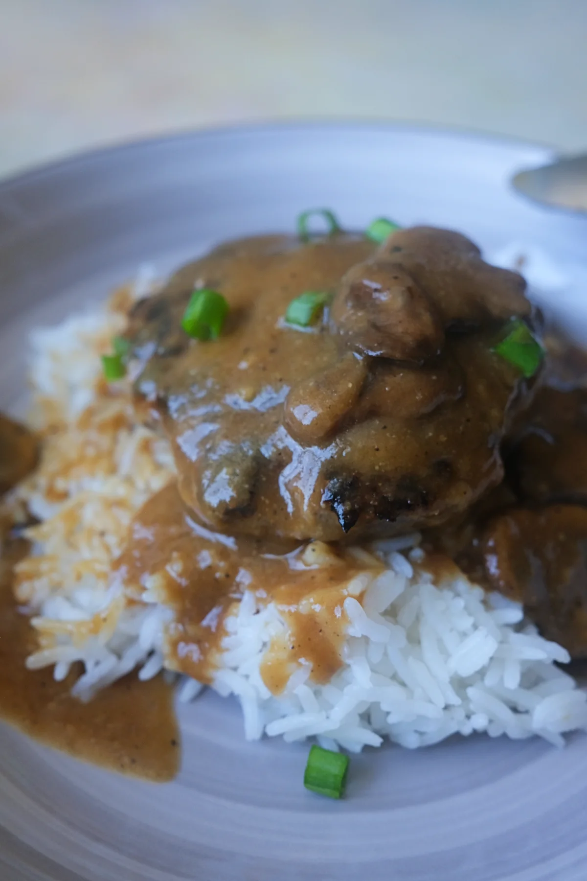 Jollibee-style burger steak served over steamed white rice with mushroom gravy spooned on top.