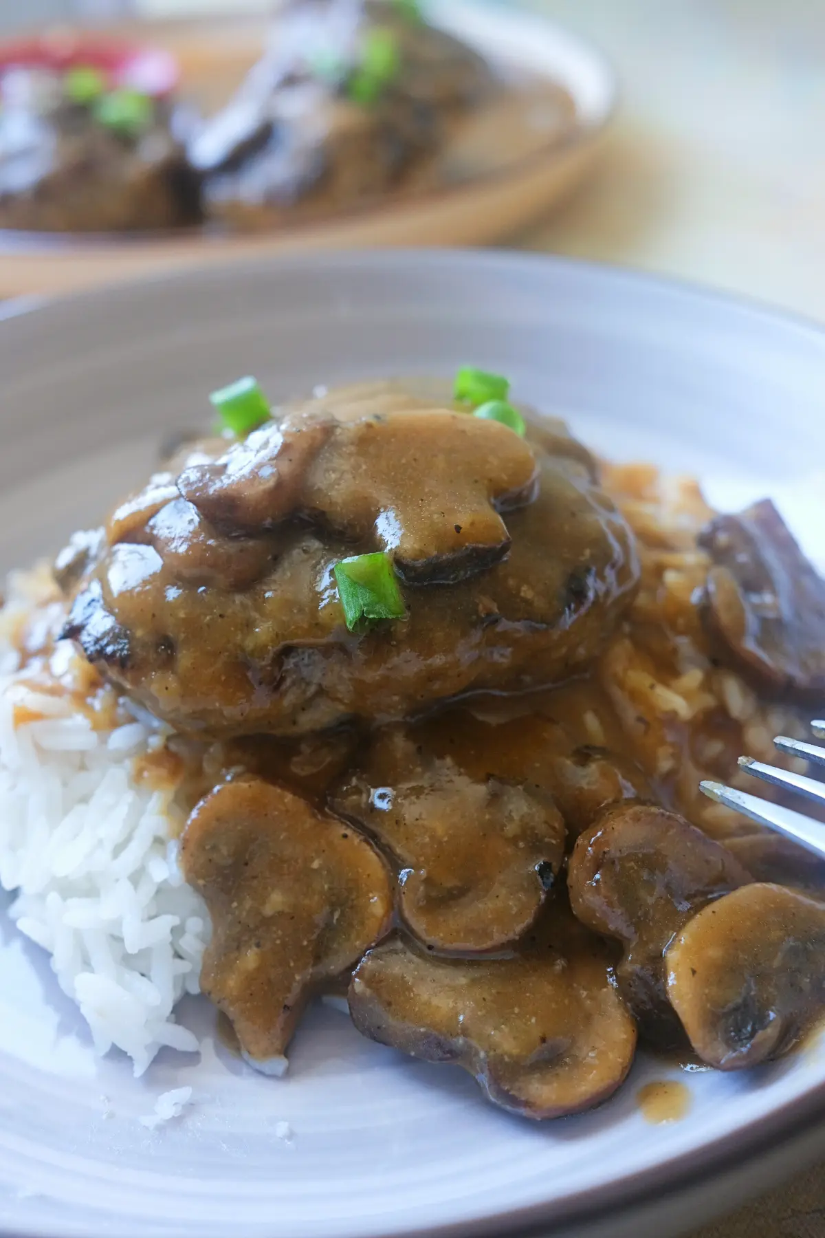 Close-up of hamburger steak with mushroom gravy served over fluffy white rice.
