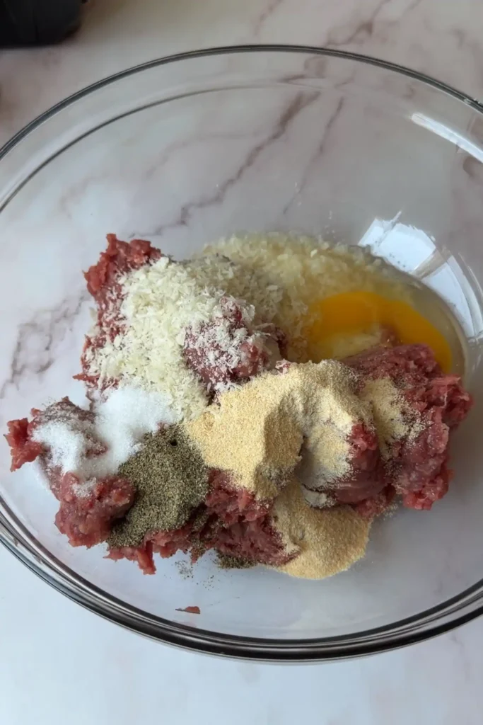 Ground beef mixture with egg, breadcrumbs, and seasonings in a glass bowl for homemade hamburger steak patties.