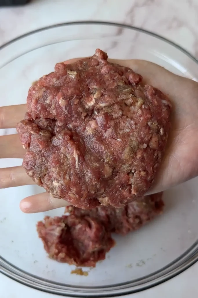 Hand shaping seasoned ground beef mixture into a thick hamburger steak patty before cooking.