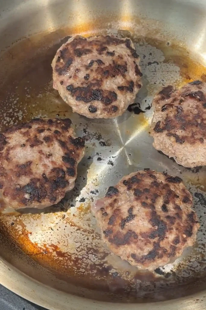 Hamburger steak patties flipped and cooked with a golden brown crust on the outside.