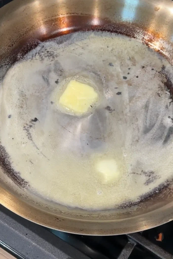 Butter melting in the same skillet with browned bits left from cooking hamburger steak patties.