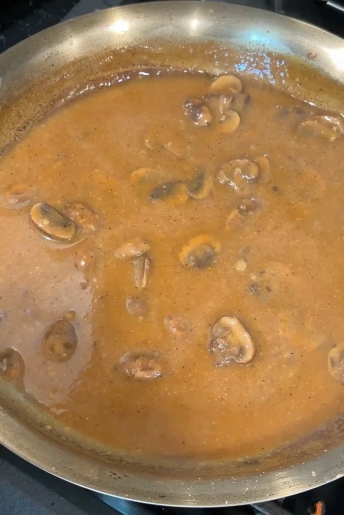 Mushroom gravy simmering in a skillet until thick and smooth for hamburger steak.
