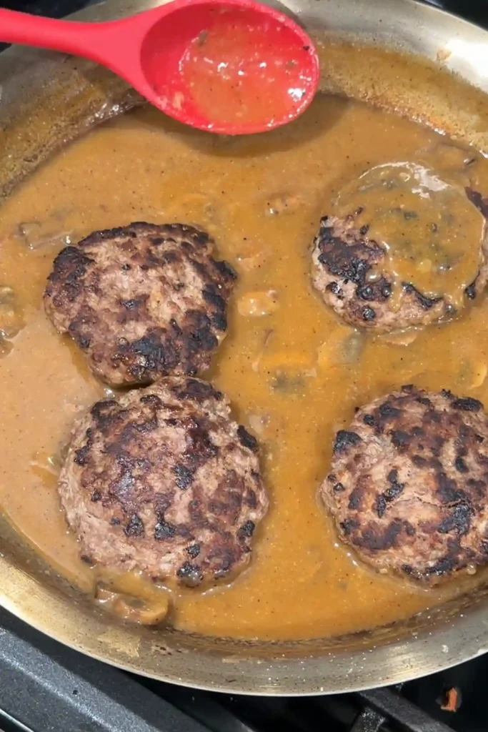 Hamburger steak patties simmering in homemade mushroom gravy with sliced mushrooms.
