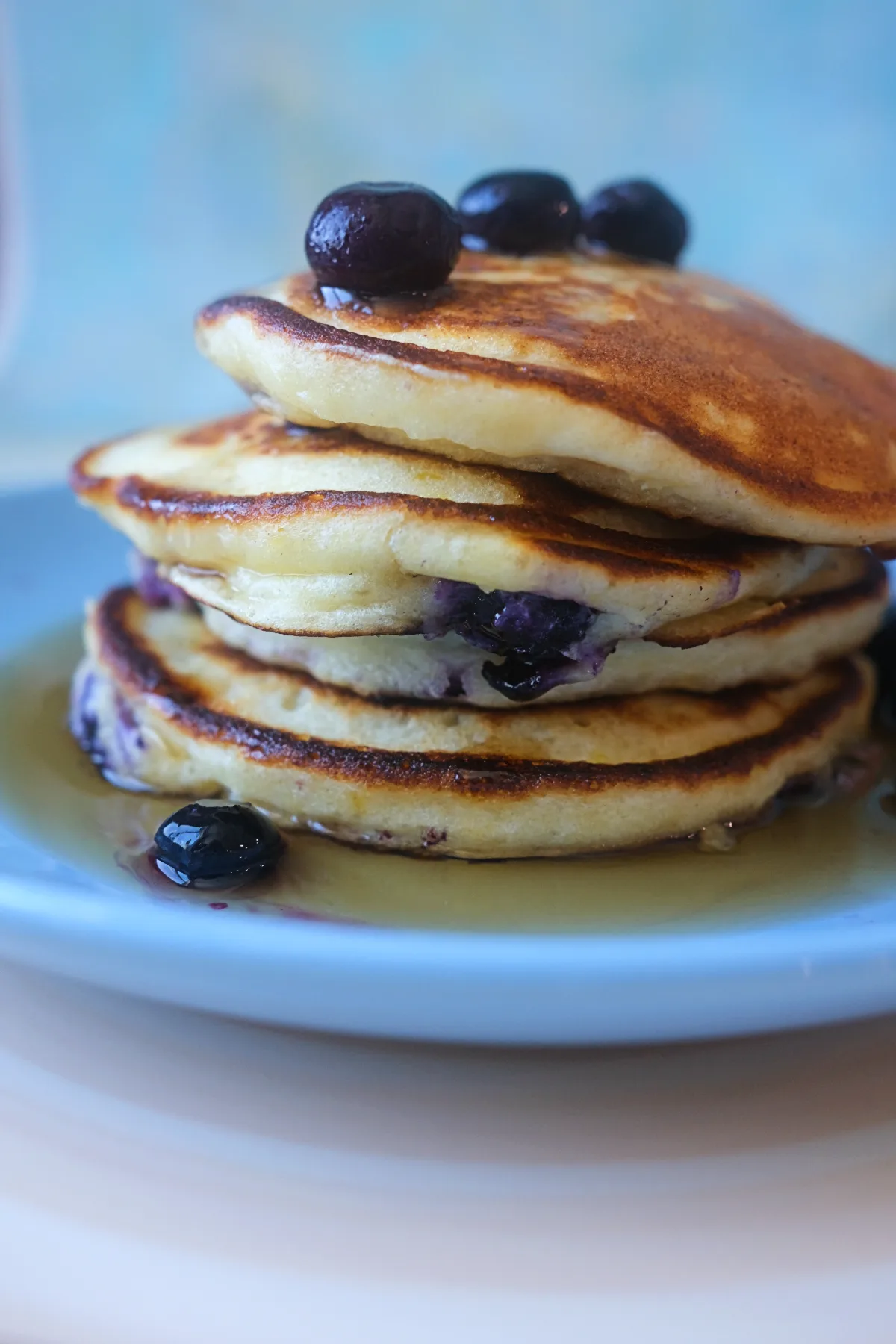 Close-up of fluffy lemon blueberry ricotta pancakes with golden edges, fresh blueberries, and maple syrup.
