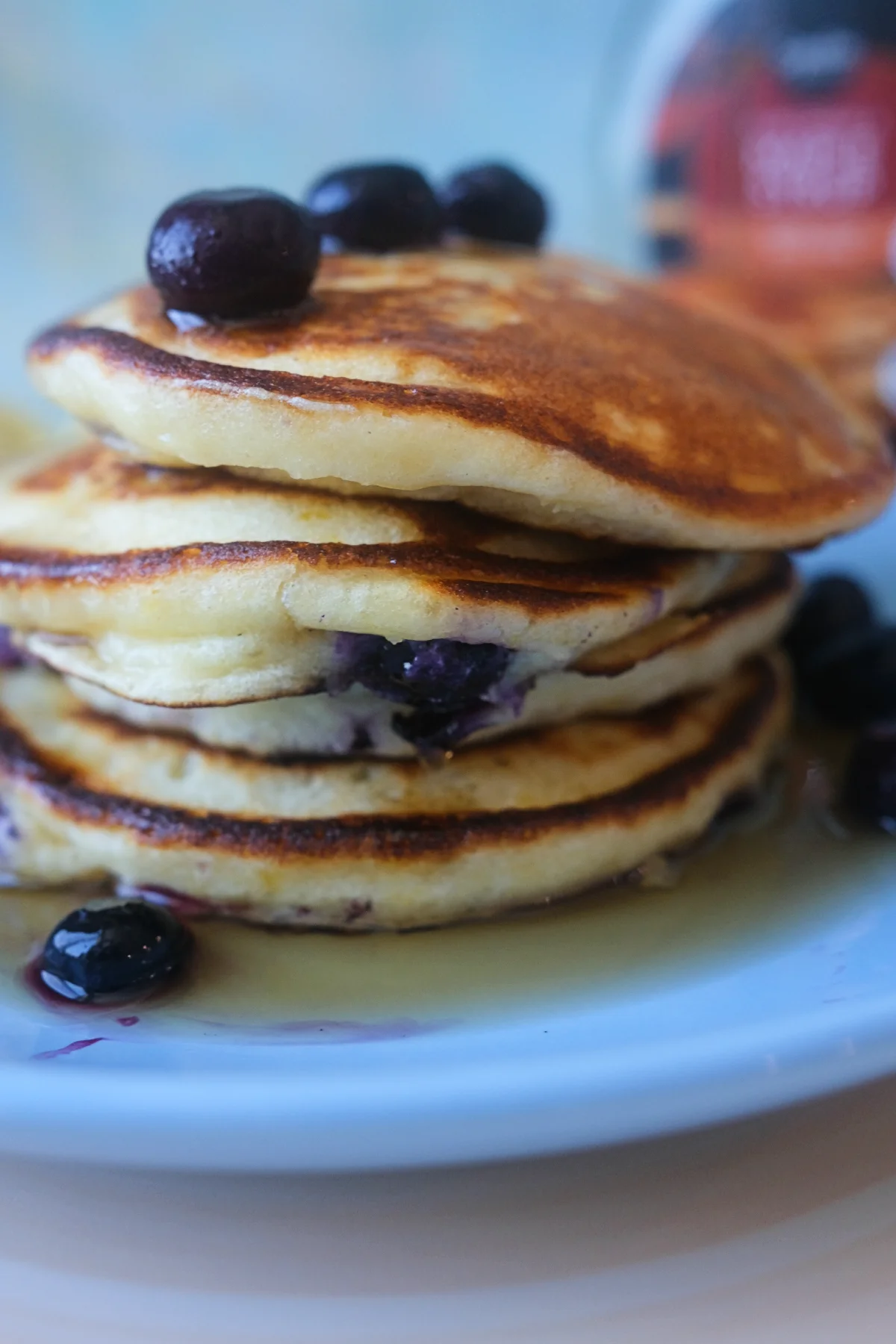 Side view of lemon blueberry ricotta pancakes with crisp golden edges, blueberries, and maple syrup.