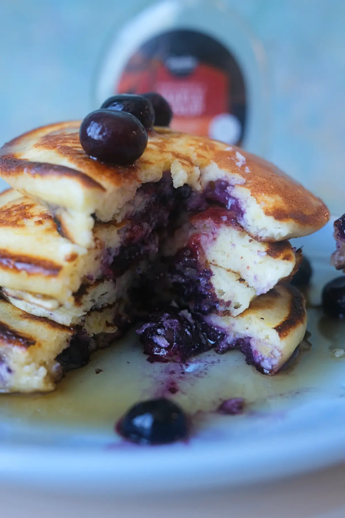 Close-up of a sliced stack of lemon blueberry ricotta pancakes with warm blueberry filling and maple syrup.